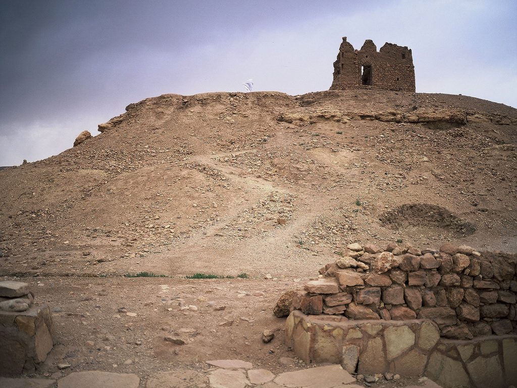 A stone building atop a hill, surrounded by a stone wall.