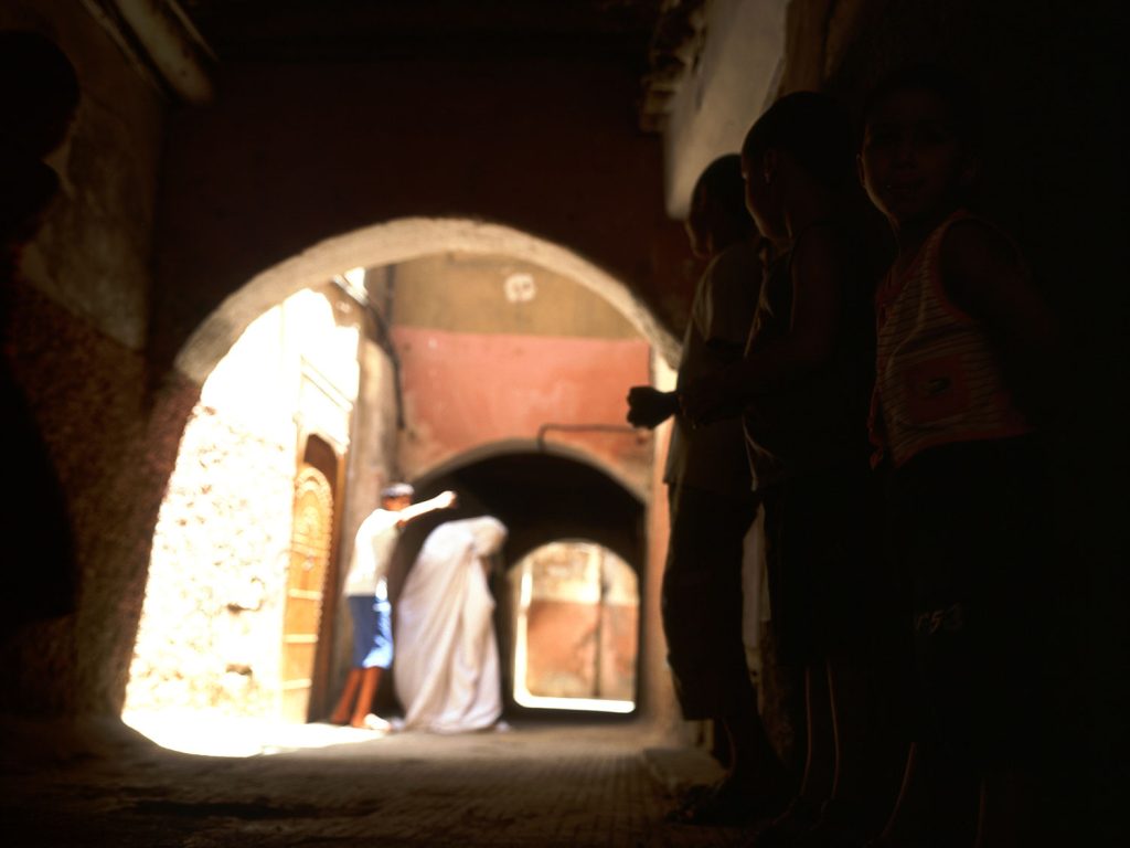 A man standing in a dimly lit alley, surrounded by shadows and mystery.