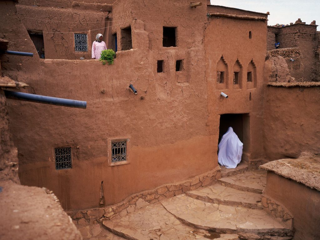 Two peoples wearing white cloths and standing on the mud house.