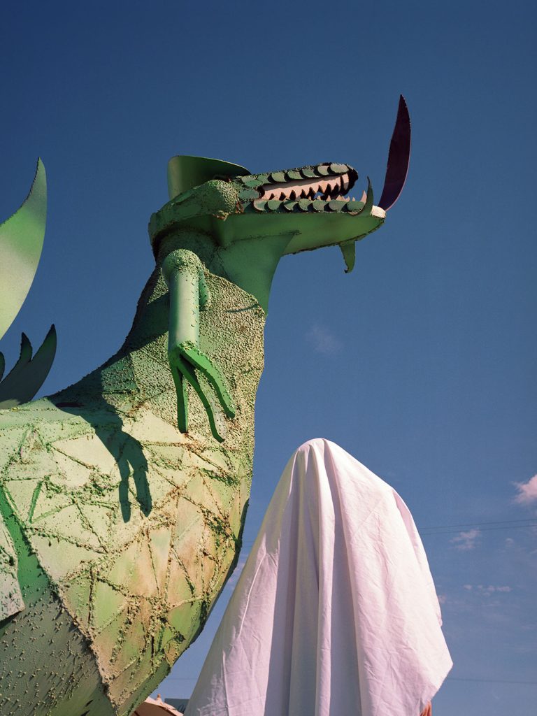 A person standing beside a massive green dragon statue, showcasing the intricate details and vibrant color.