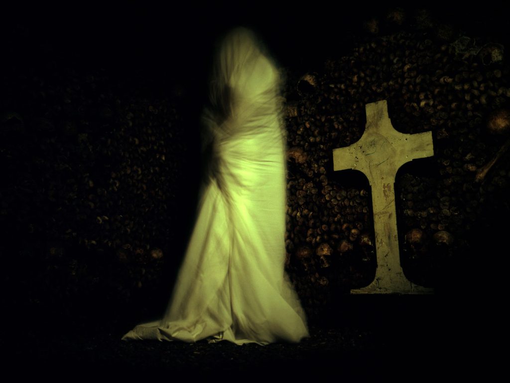 A ghostly person in a white dress standing in front of a cross, looking hauntingly beautiful.