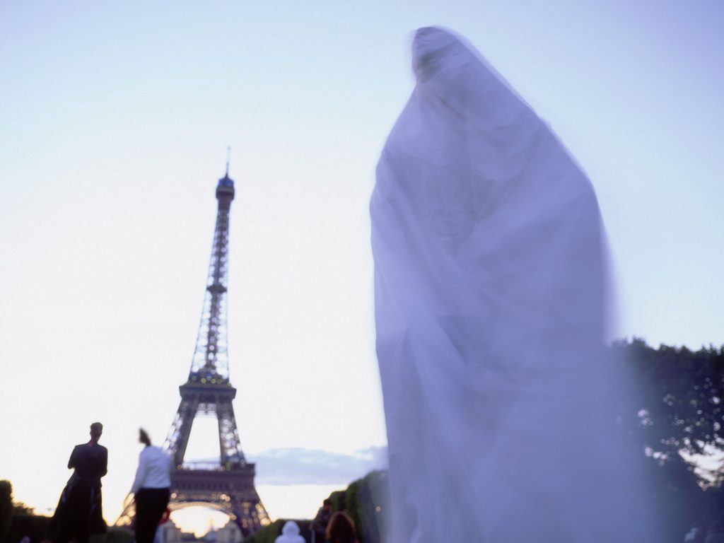 A ghostly figure in a white dress stands in front of the Eiffel Tower, creating an eerie and captivating scene.