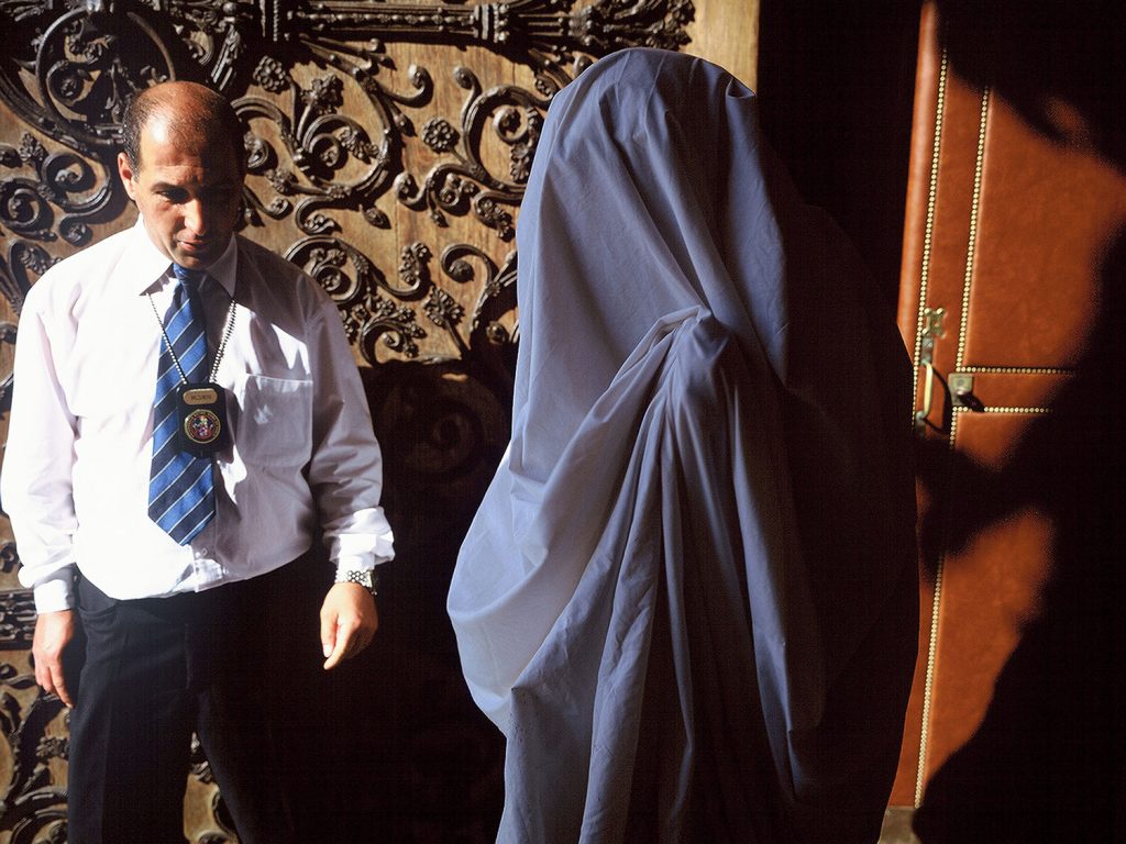 There is a man wearing a suit and tie standing alongside a personwho is wearing a veil.