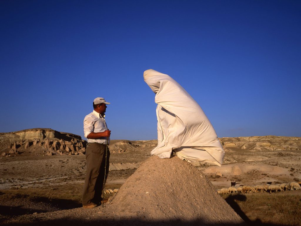 A person standing on a mound with a white robe draped over it, overlooking a serene landscape.