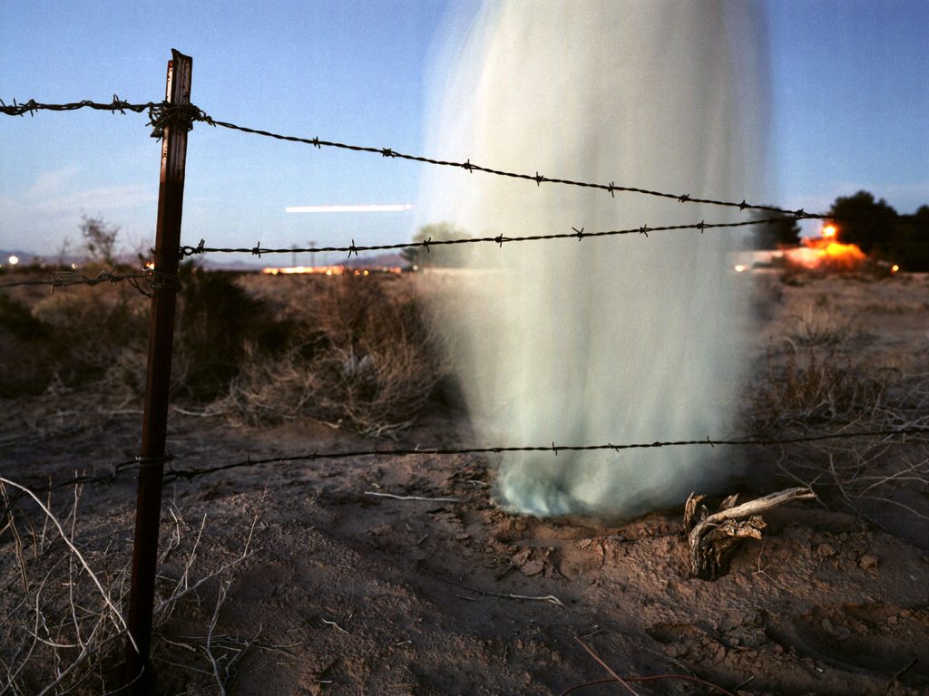 A blue cloud drifts before a barbed wire fence, creating a serene yet guarded atmosphere.