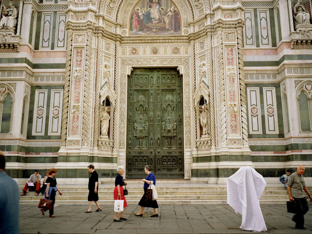 People walking in front of a large building with a white ghost statue.