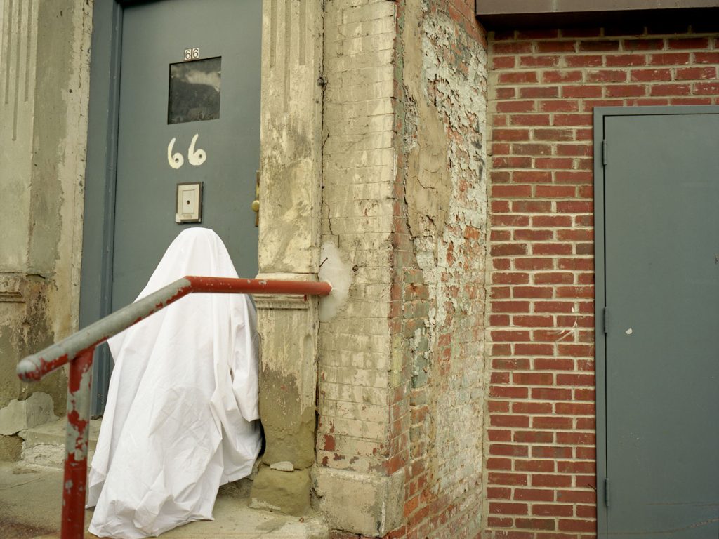 A ghostly figure standing in front of a door, appearing translucent and eerie.