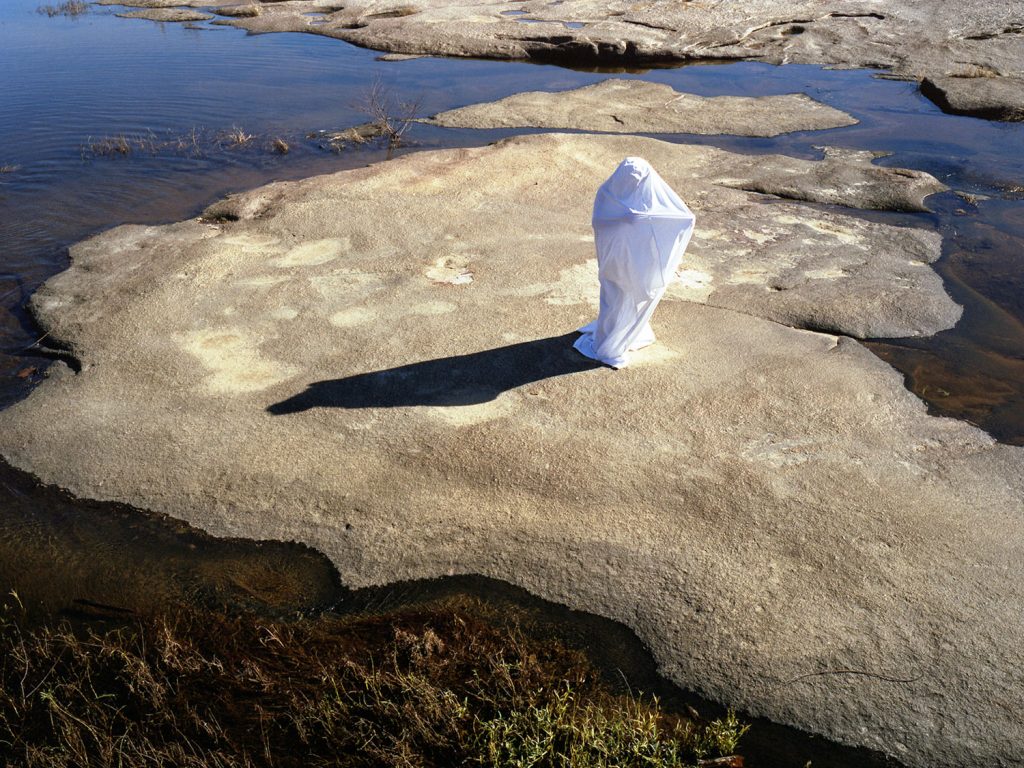 A person draped white cloth stand on rock, creating a serene and elegant scene.