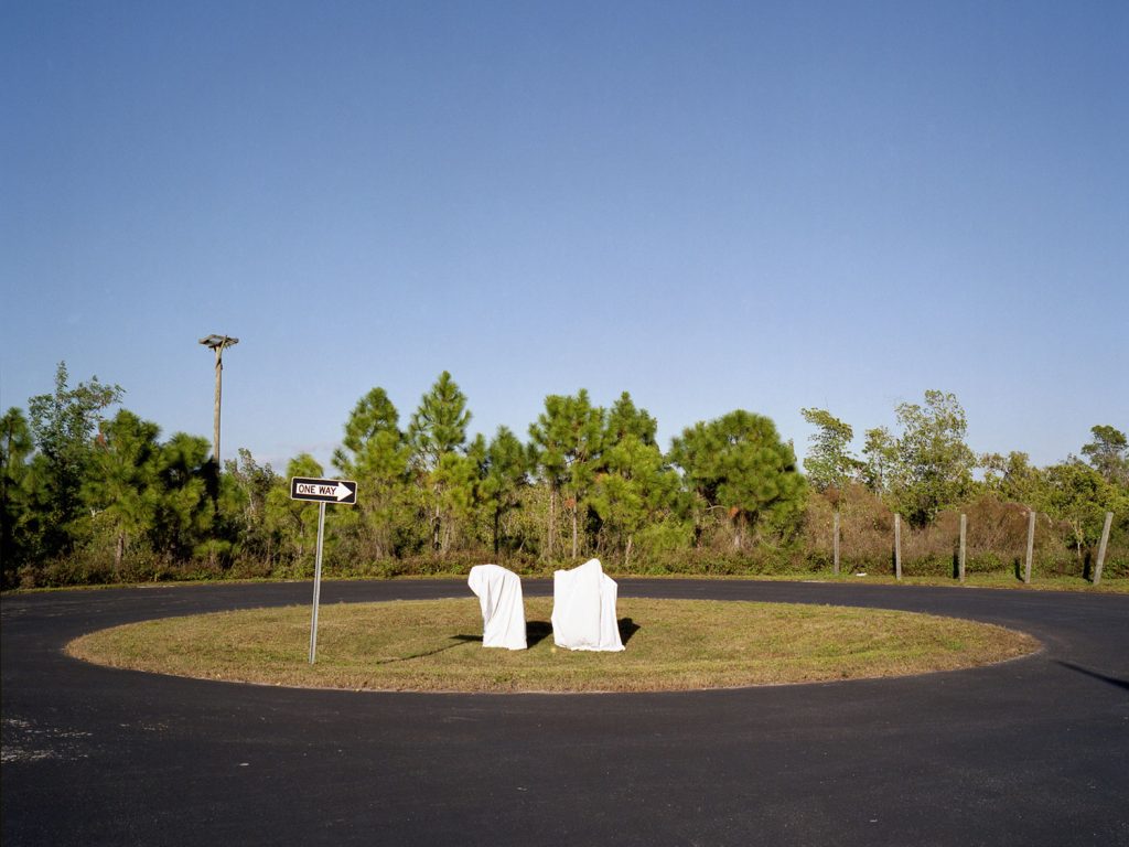 A white sign with a ghost emblem stands in the center of a parking lot, creating an eerie and mysterious atmosphere.