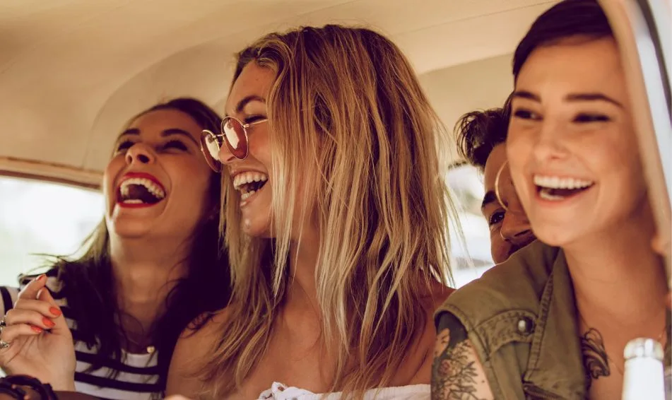 Three women joyfully laughing together inside a car, showcasing a moment of friendship and fun